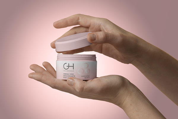 mano che tiene una confezione di crema per il viso adatta per pelli impure